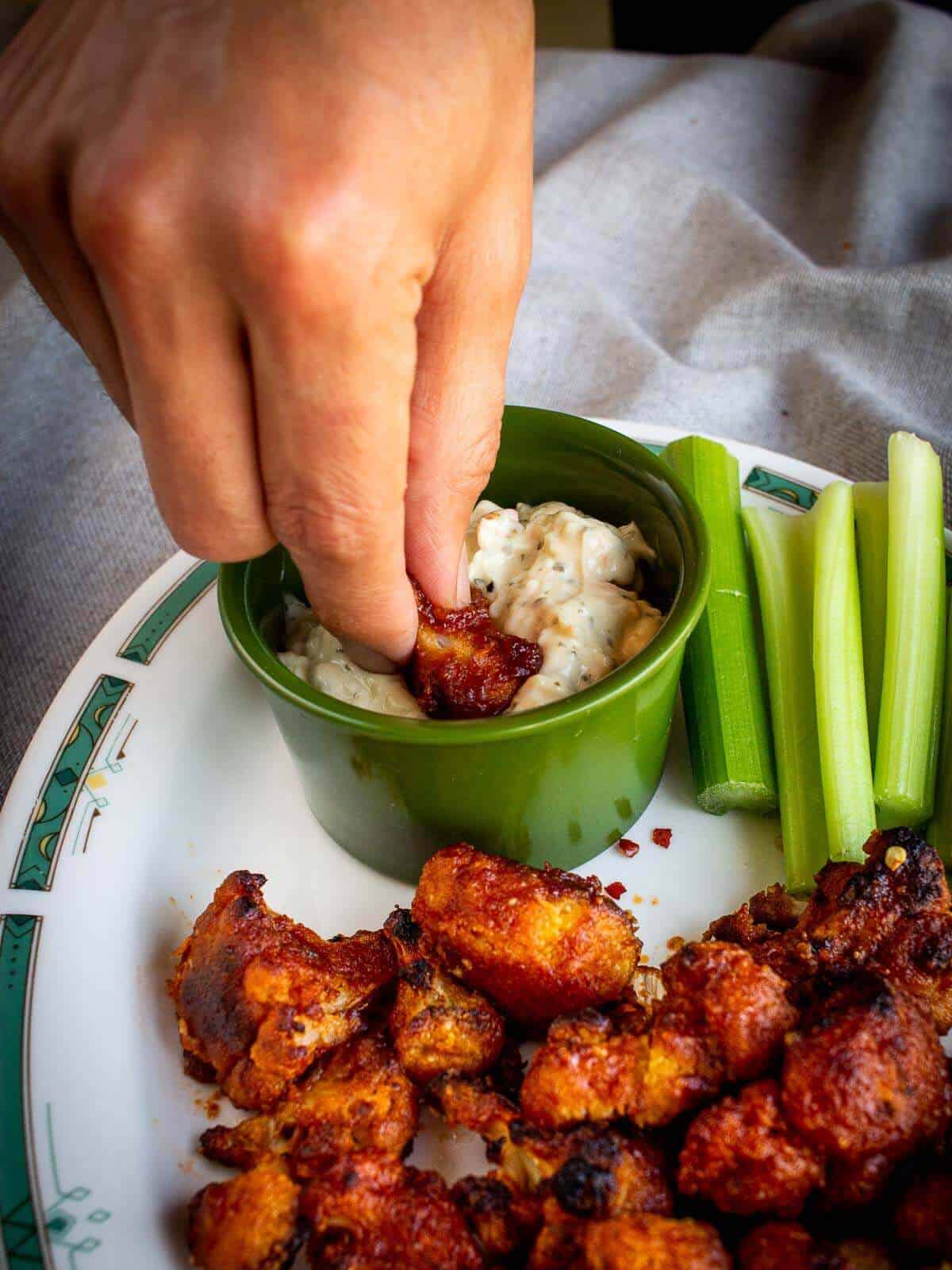 dipping vegan cauliflower wings in sauce.