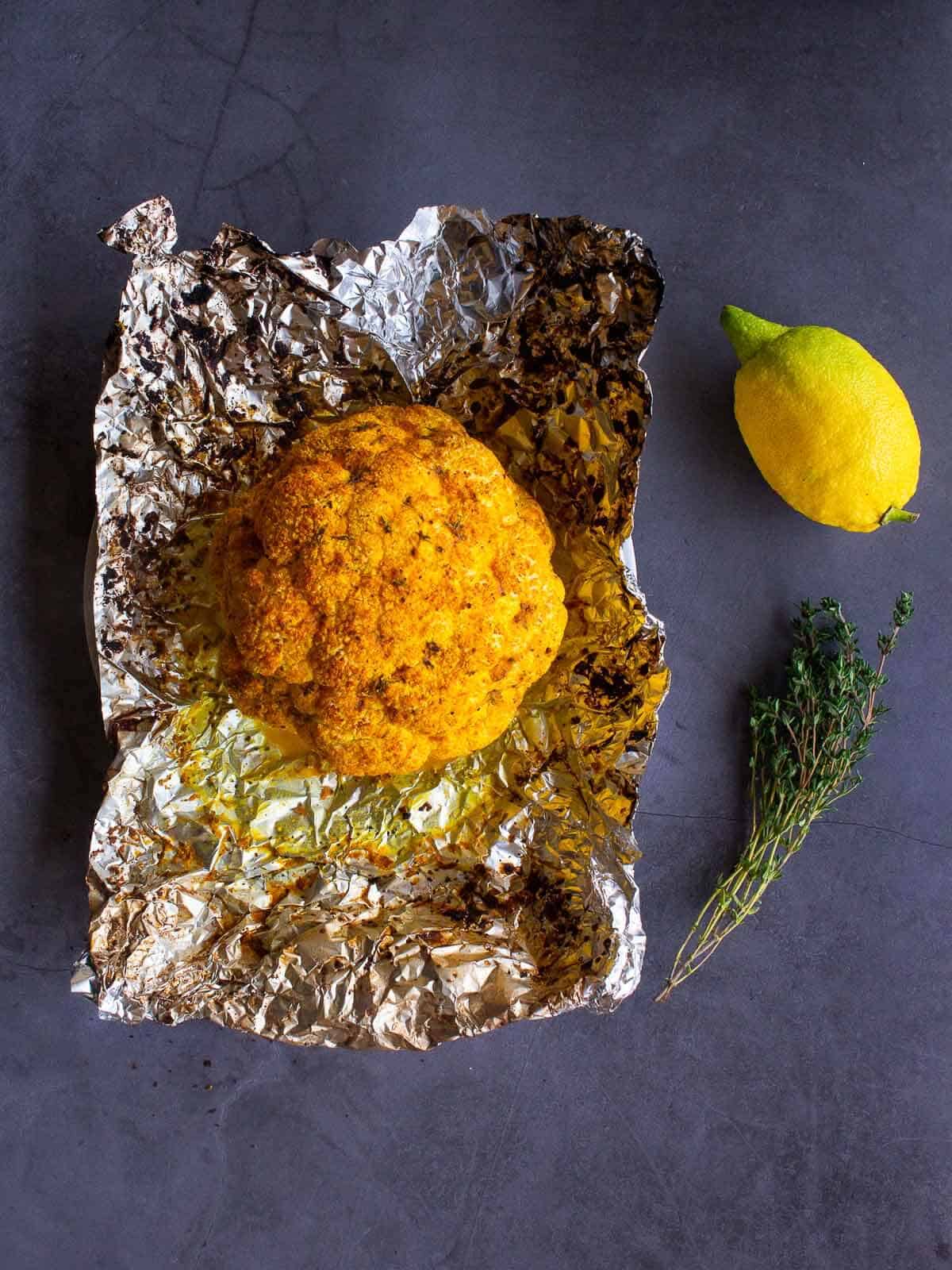 Spiced Roasted Cauliflower on an opened aluminium foil next to a lemon and thyme sprigs.