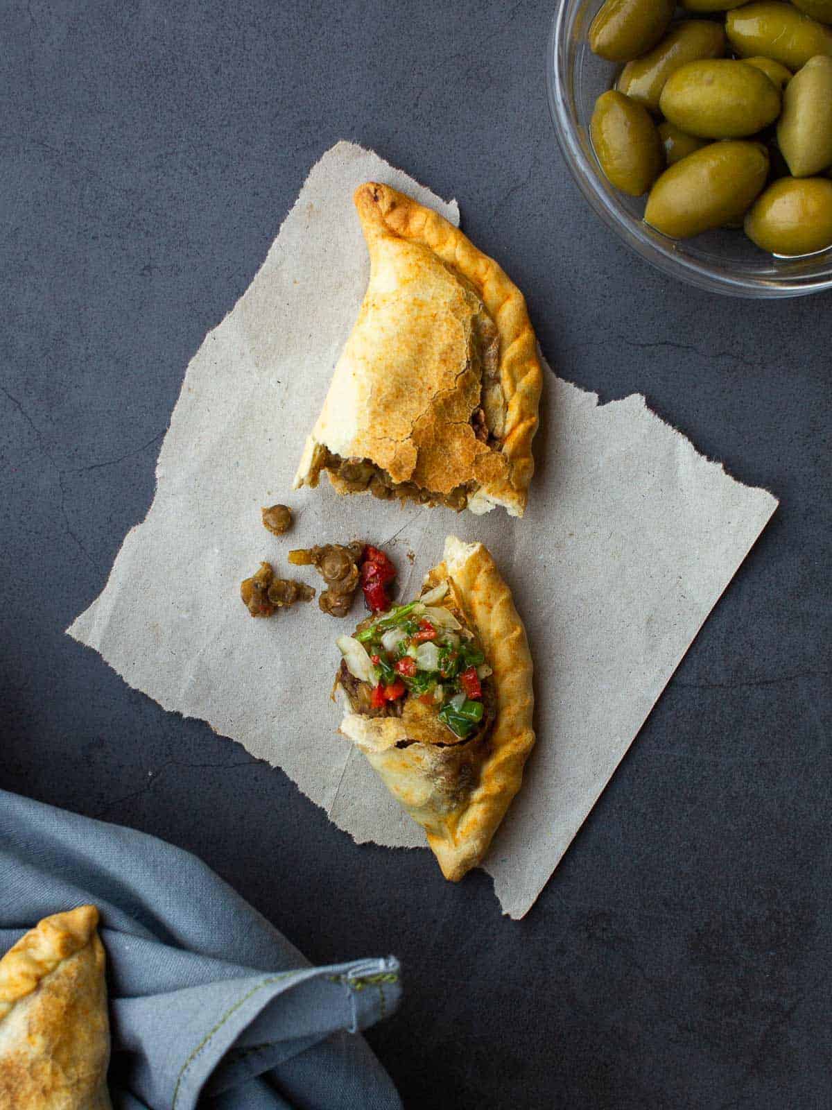 Halved Vegan Empanada served with green olives.