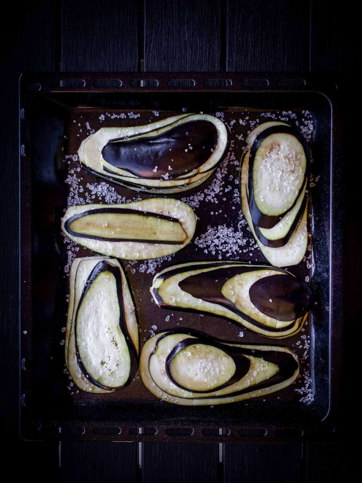 eggplant slices in baking sheet with coarse salt on top.