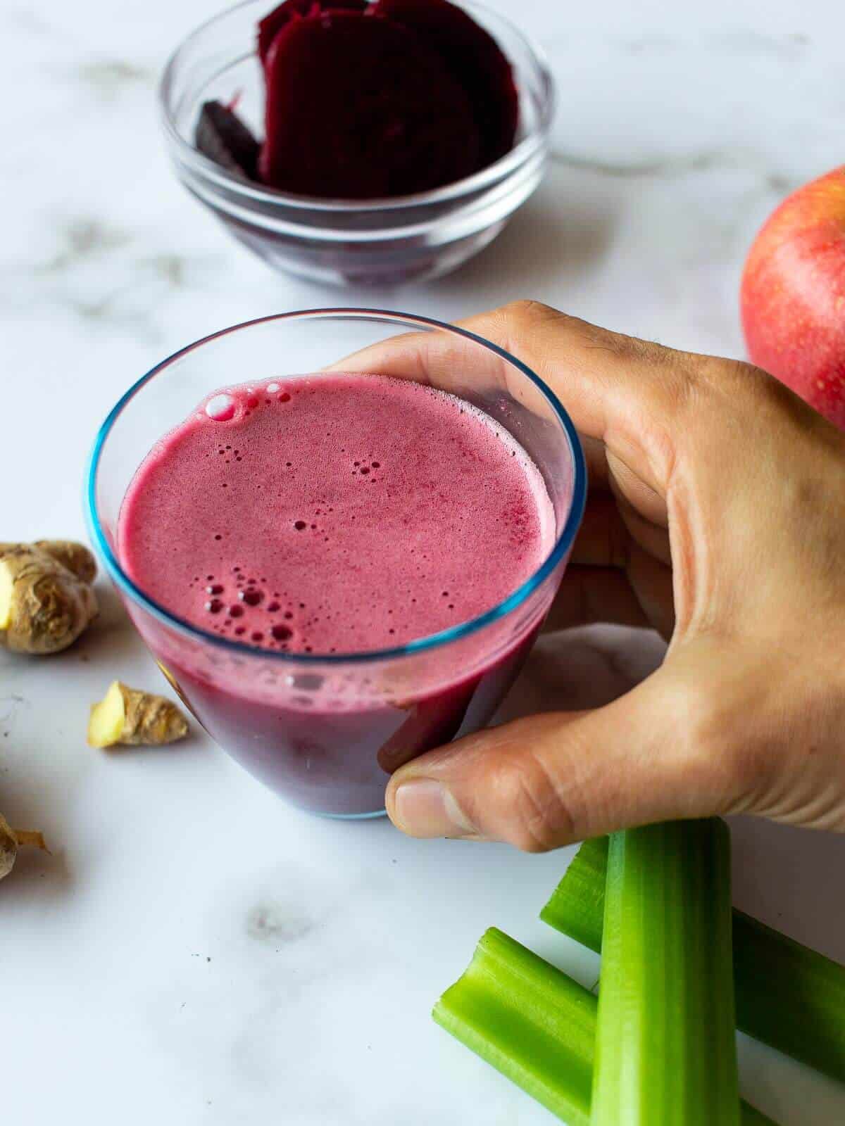 hand holding a beetroot and celery glass of juice