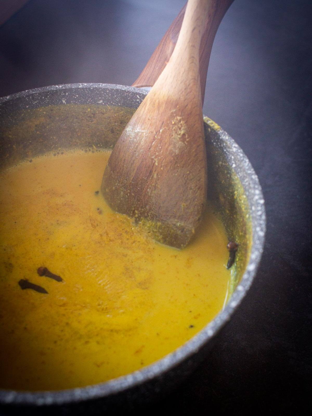 whisking simmering golden milk in a saucepan.