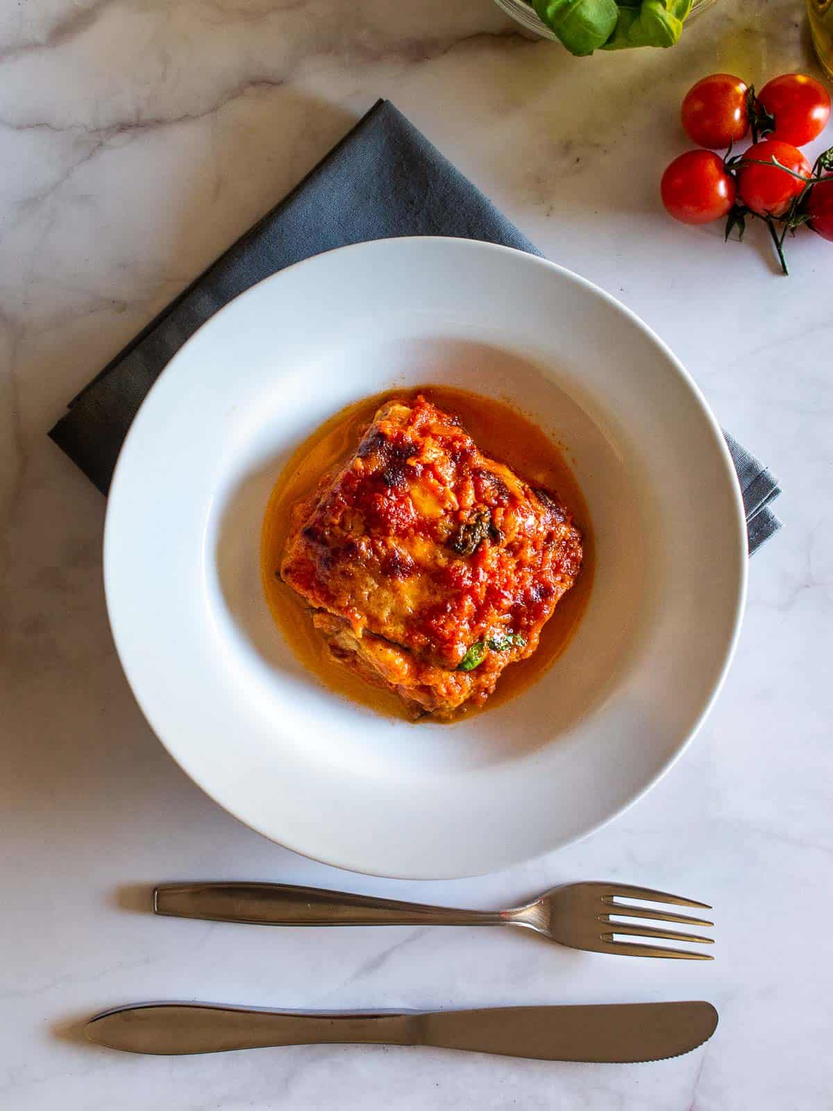 eggplant parmesan served in a white plate with a fork.