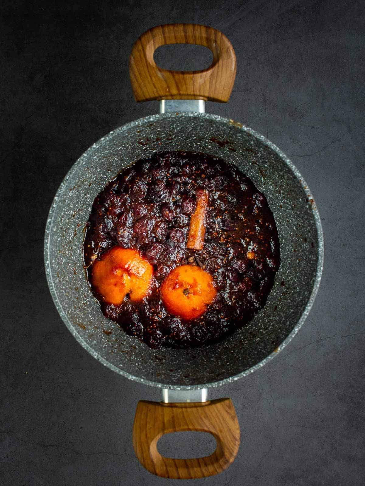 Cranberry Sauce boiling in a saucepan with clementine and cinnamon sticks.