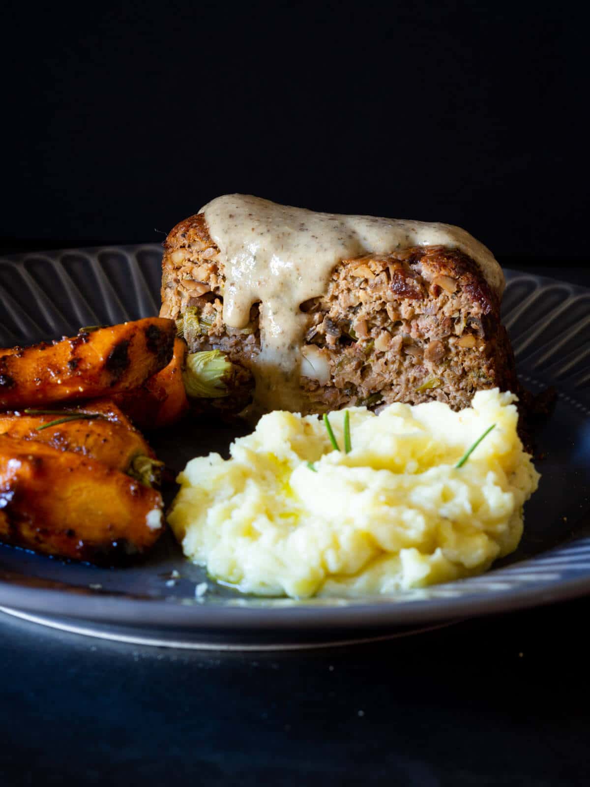 vegan mushroom gravy on top of a vegan nut roast served with mashed potatoes and maple glazed carrots.