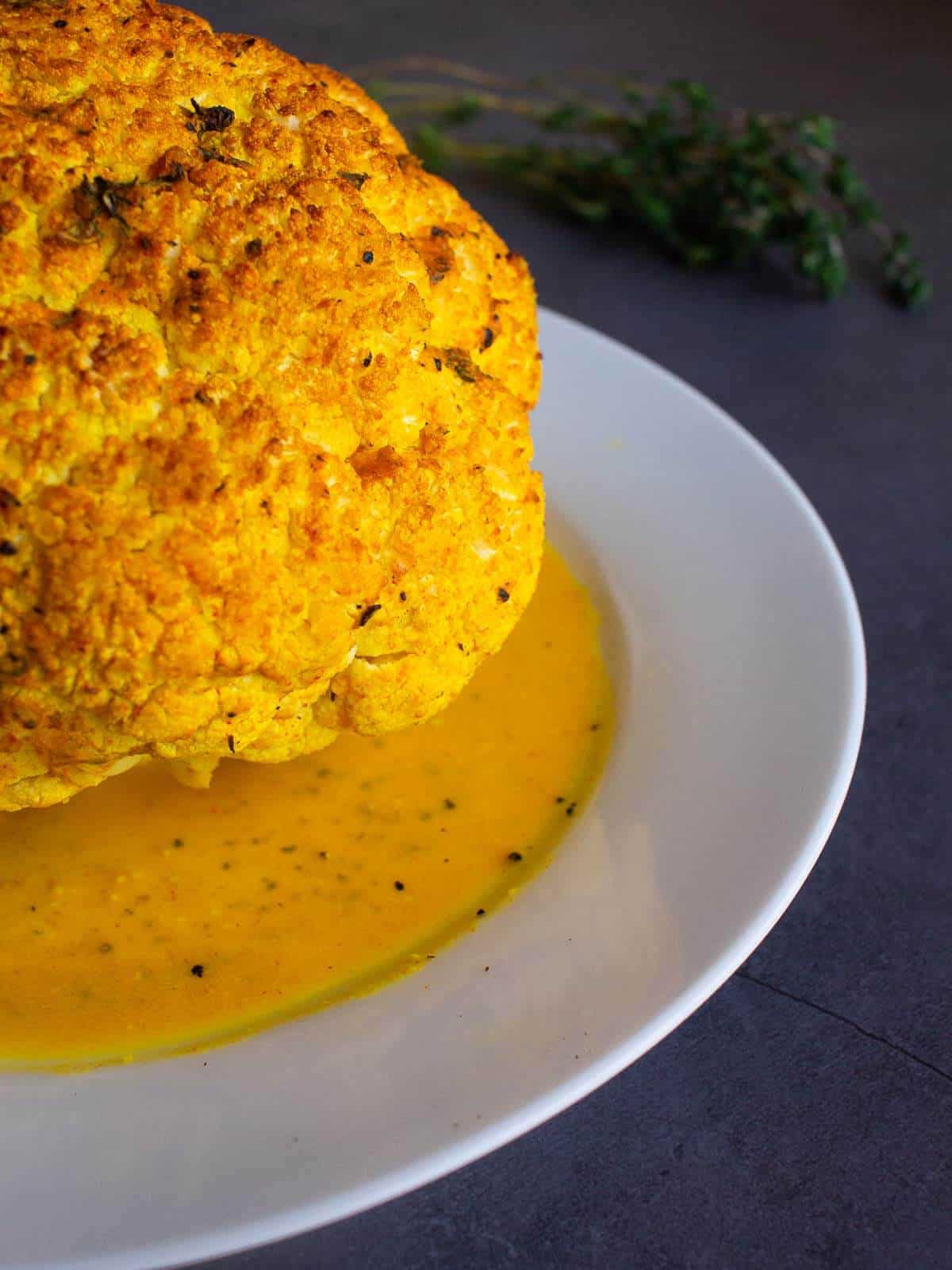 Spiced Roasted Cauliflower with tahini served with all its juices on a white serving plate.