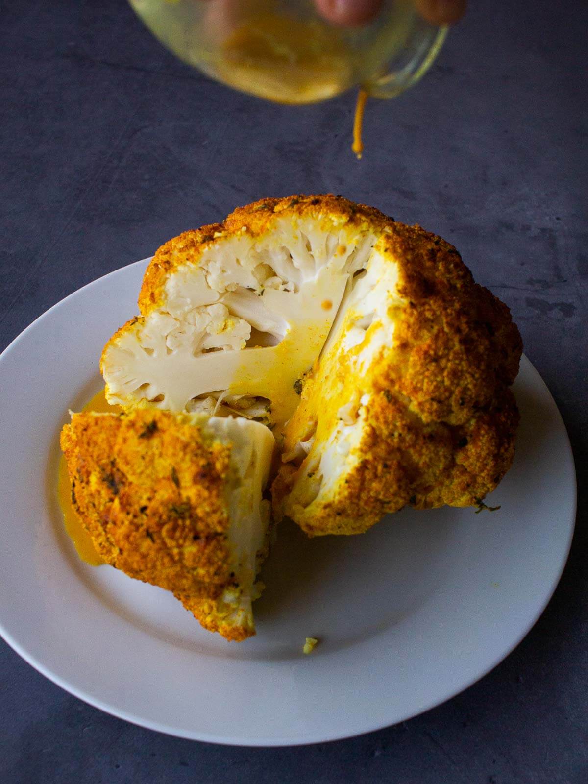 pouring tahini sauce over the baked head of Roasted Cauliflower.