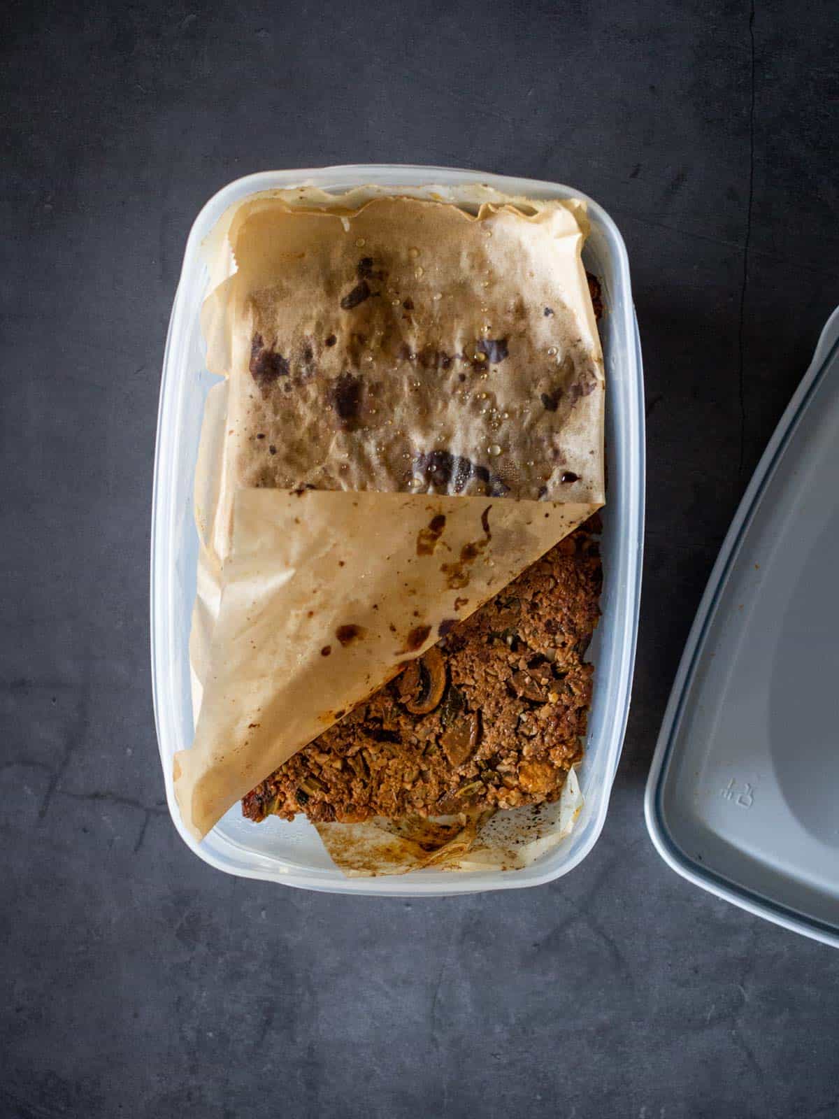 vegan roast stored in airtight container with parchment paper on top and bottom.