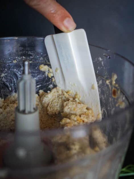 scraping edges of food processor with a spatula.