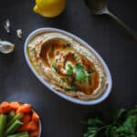 Lebanese hummus served on a plate with a bowl of carrot and celery sticks.