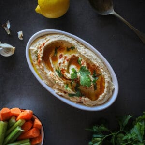 Lebanese hummus serves on a plate with a bowl of carrot and celery sticks.