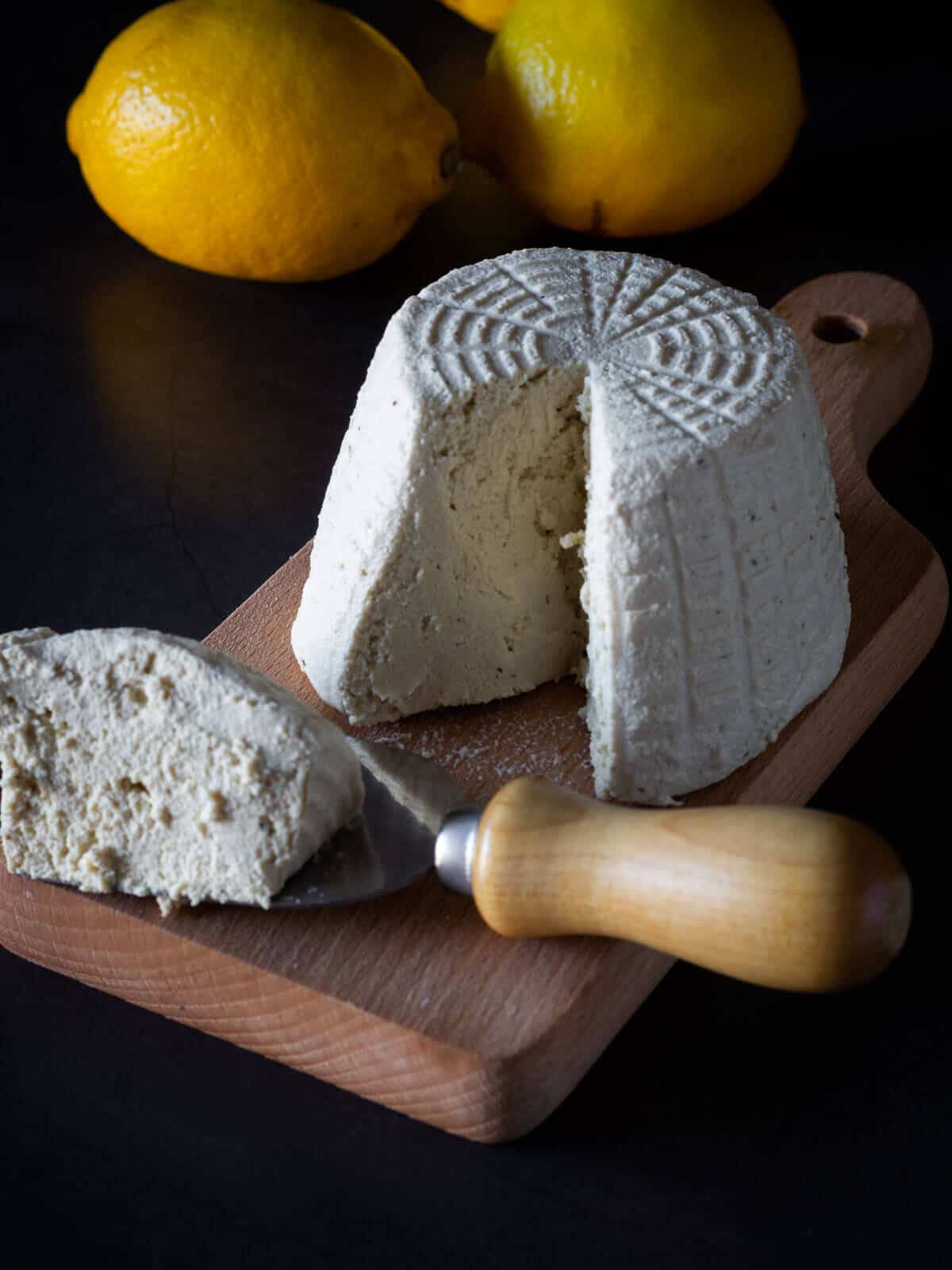 dairy-free ricotta cheese on a serving wooden cheese table, shaped sliced with a cheese cutter