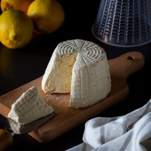 vegan ricotta on a serving wooden cheese table, shaped sliced with a cheese cutter