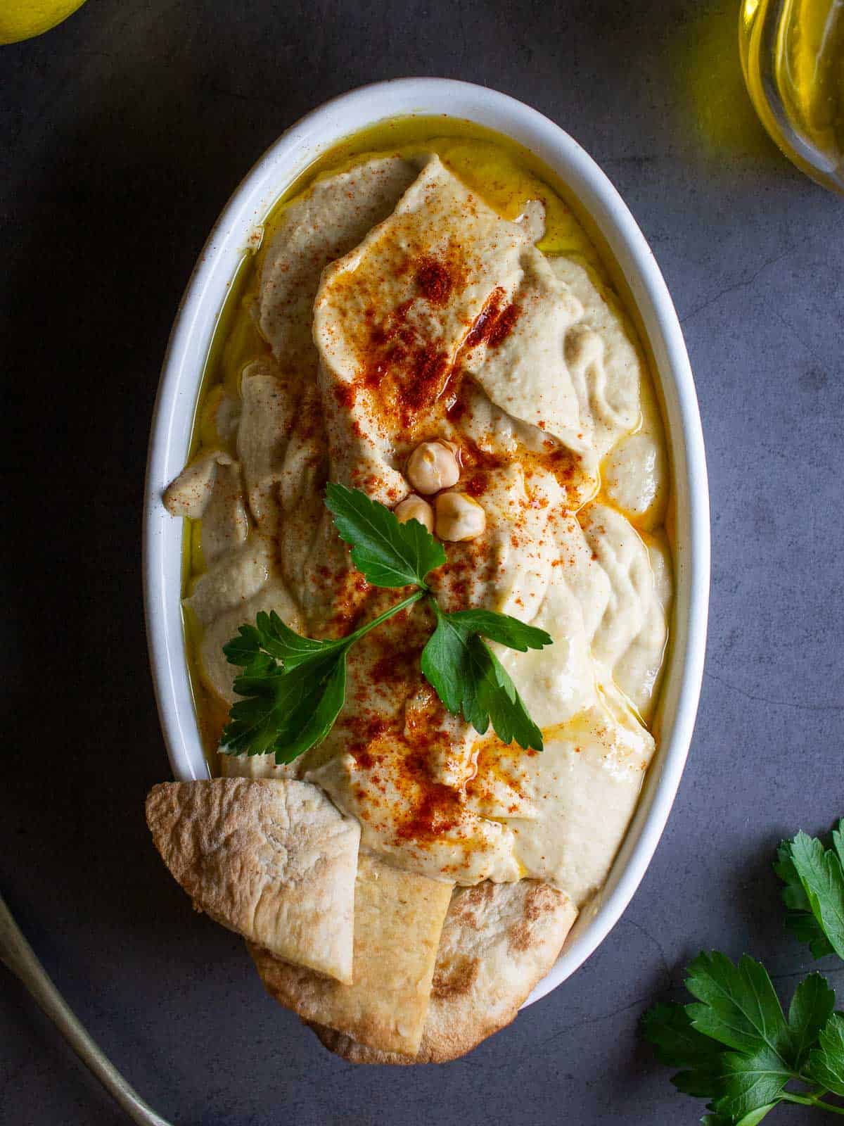 classic Hummus served on an oval plate garnished with paprika, pita chips and flat parsley.