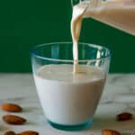 pouring homemade almond milk into a glass.