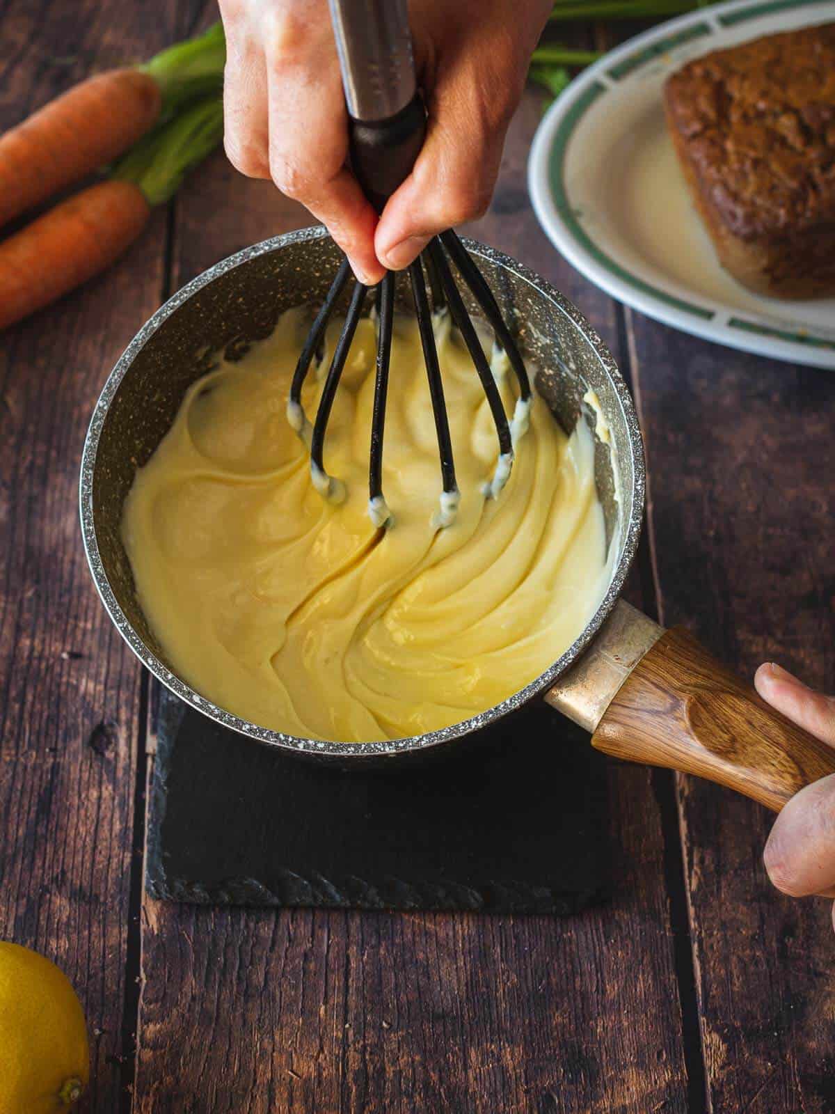 whisking vegan buttercream frosting on top of carrot cake