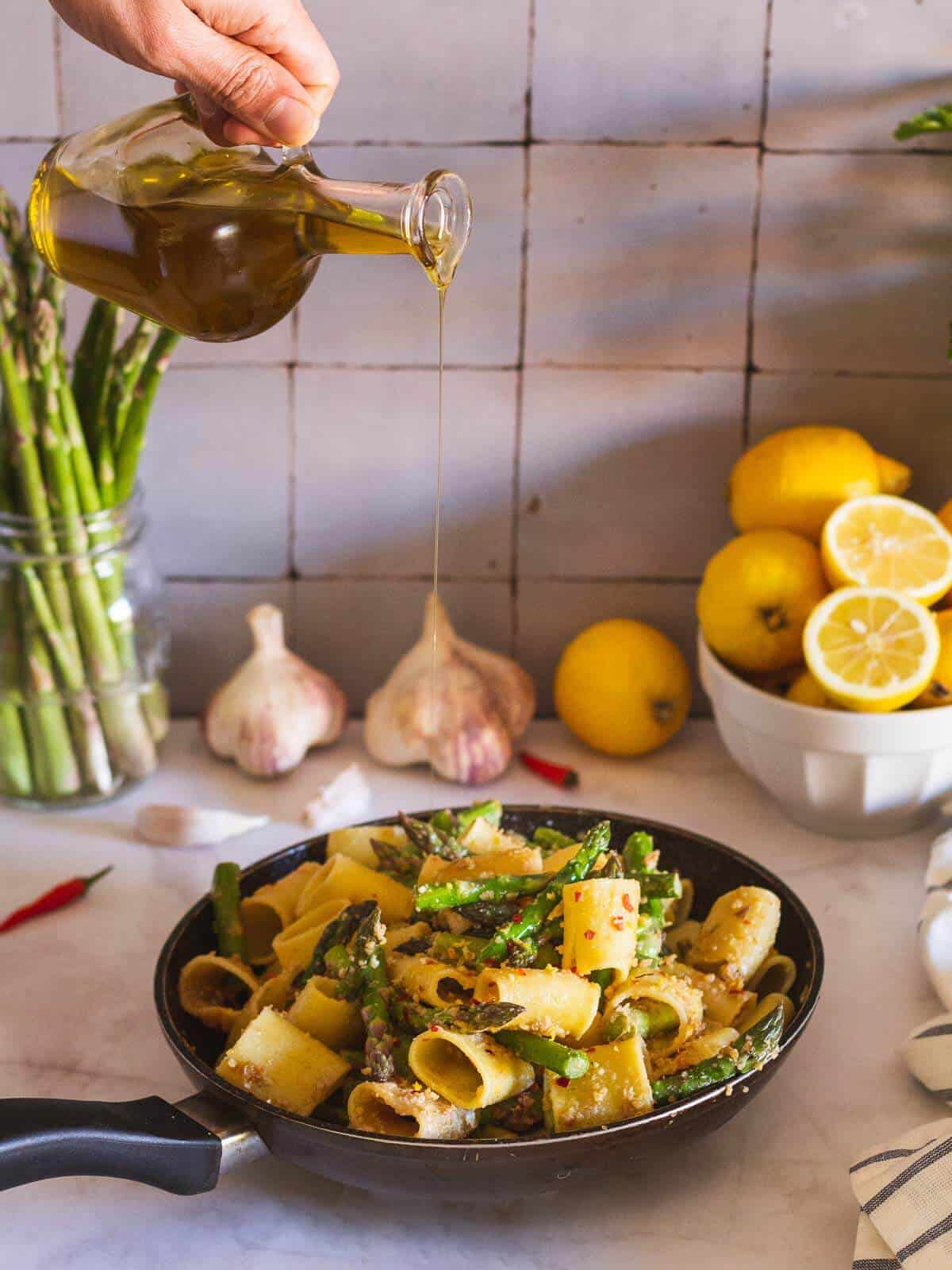 adding olive oil to pasta with asparagus in a skillet
