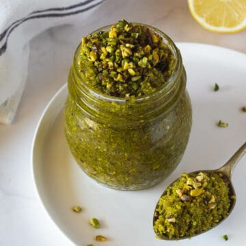 vegan pistachio pesto in airtight container next to a spoon of pesto