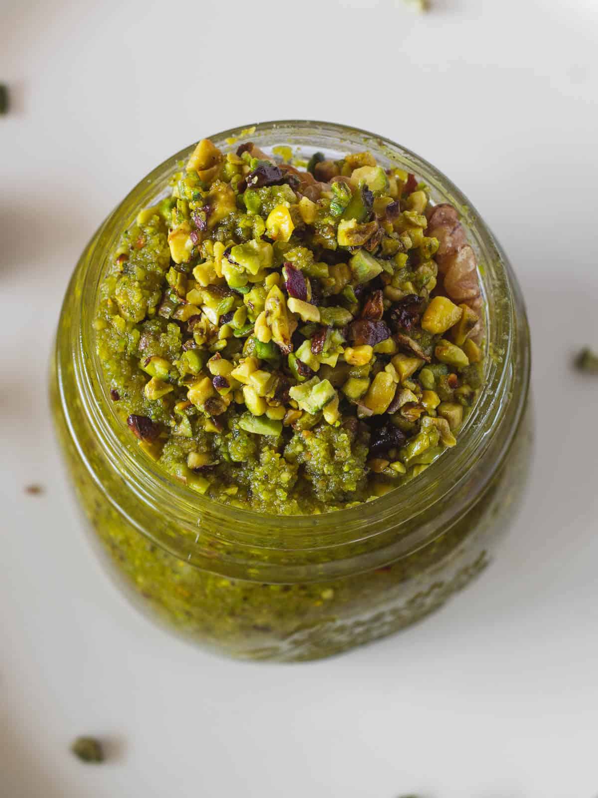 vegan pistachio pesto in airtight container next to a spoon of pesto