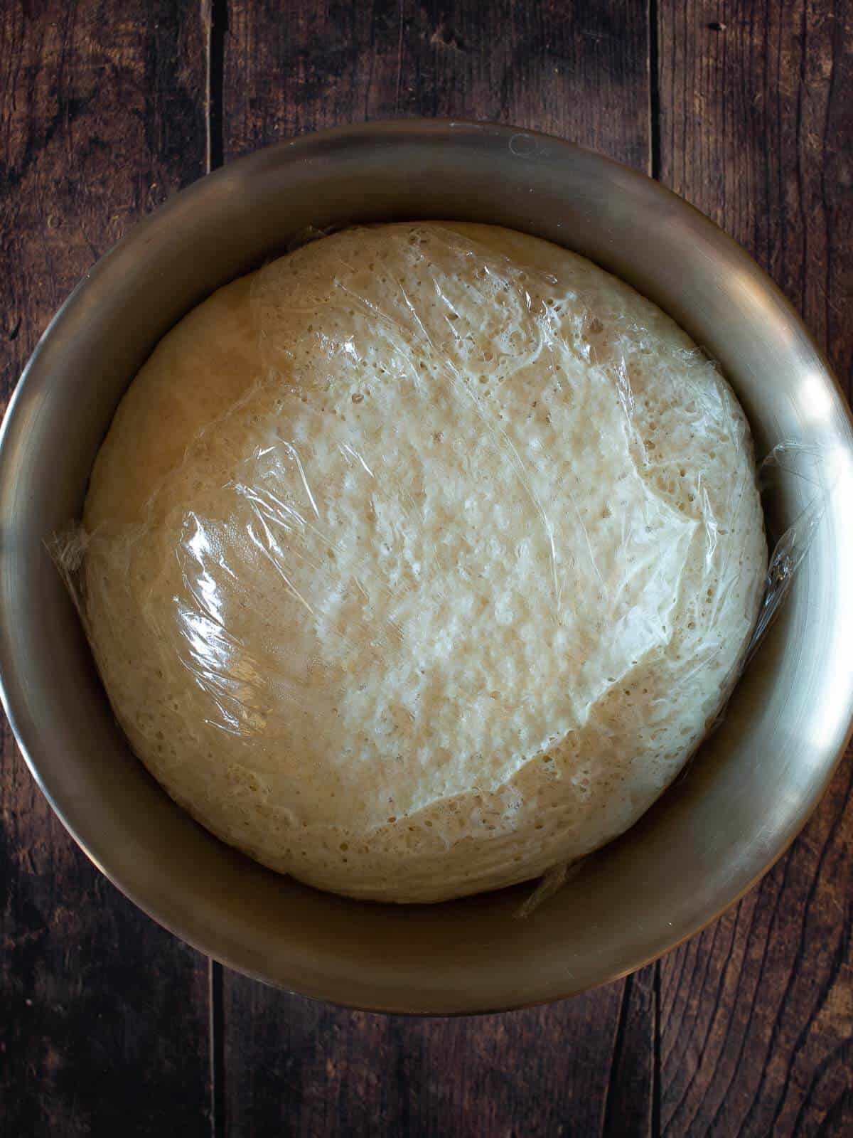 vegan pizza dough after rising with plastic wrap on top