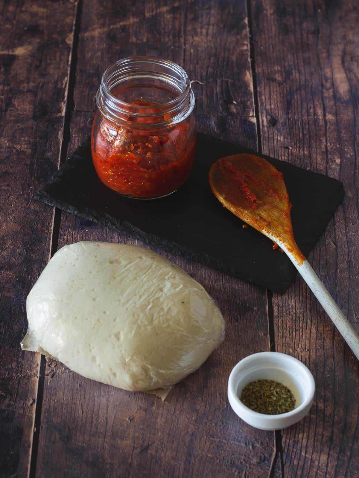 pizza sauce next to pizza dough ball wrapped on cling