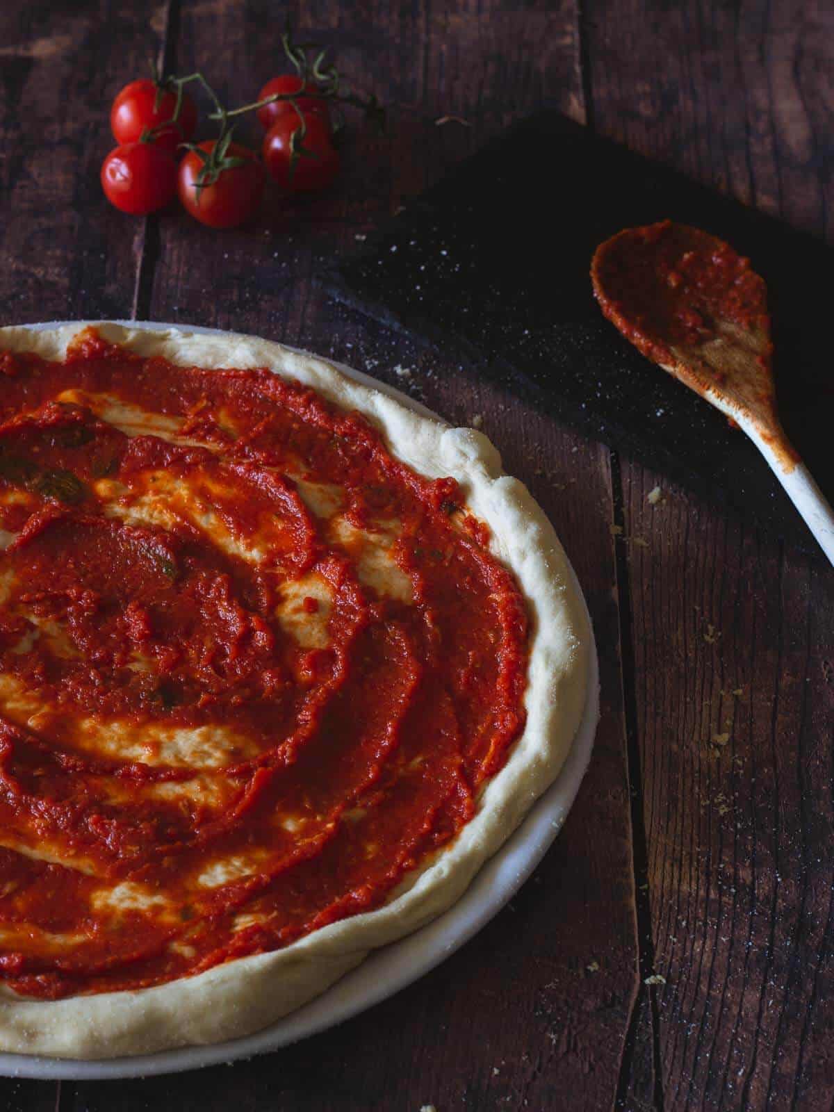 vegan pizza dough extended with tomato sauce on top.