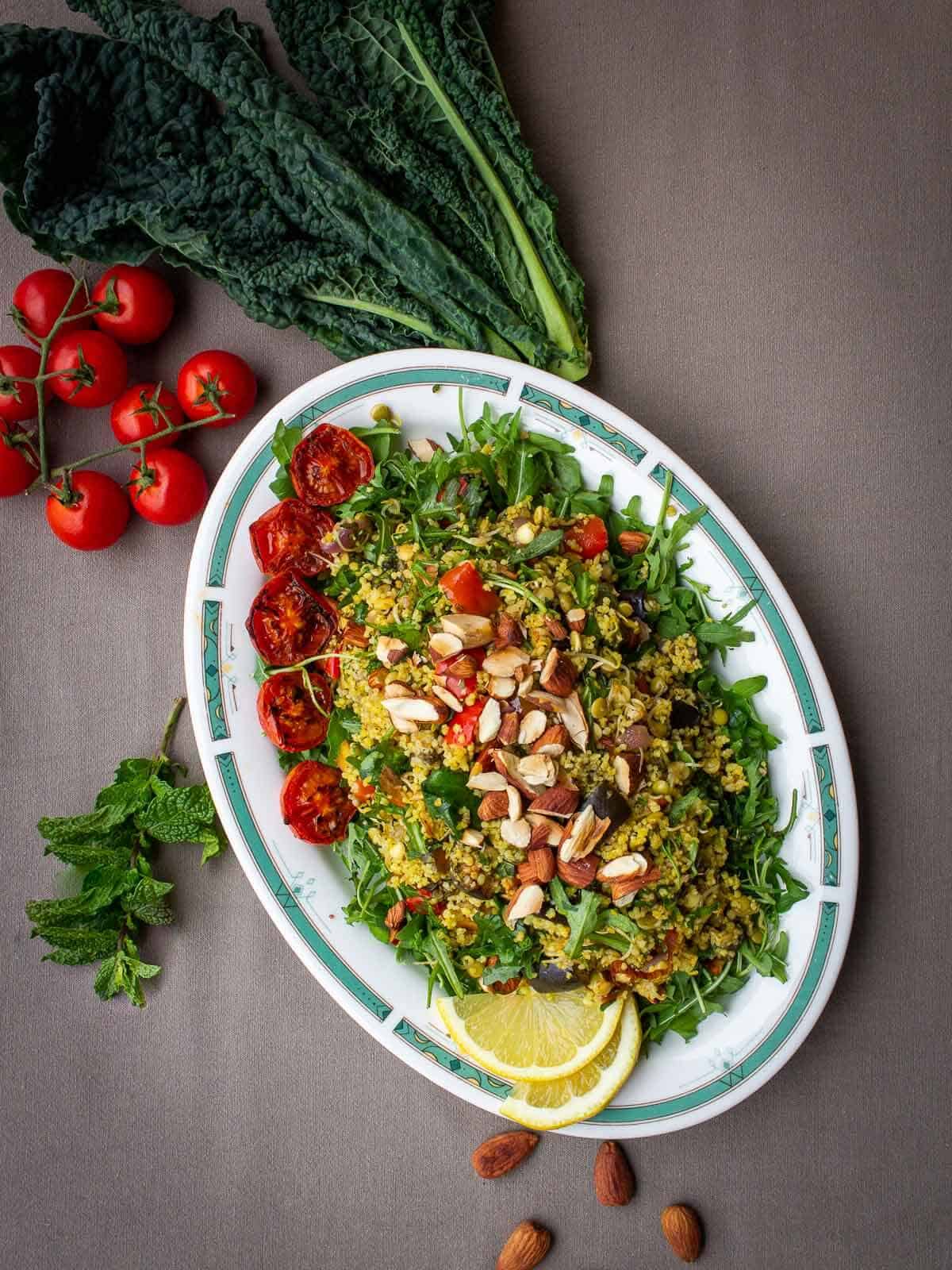 ensalada tibia de couscous servida en un plato ovalado con almendras tostadas encima y tomates cherry.