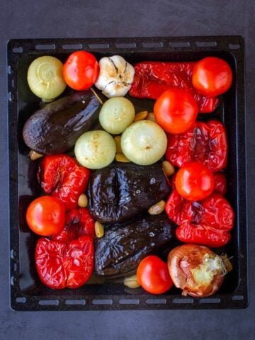 half-cooked onions, eggplants, garlic, and pepper in a tray, plus added raw tomatoes.