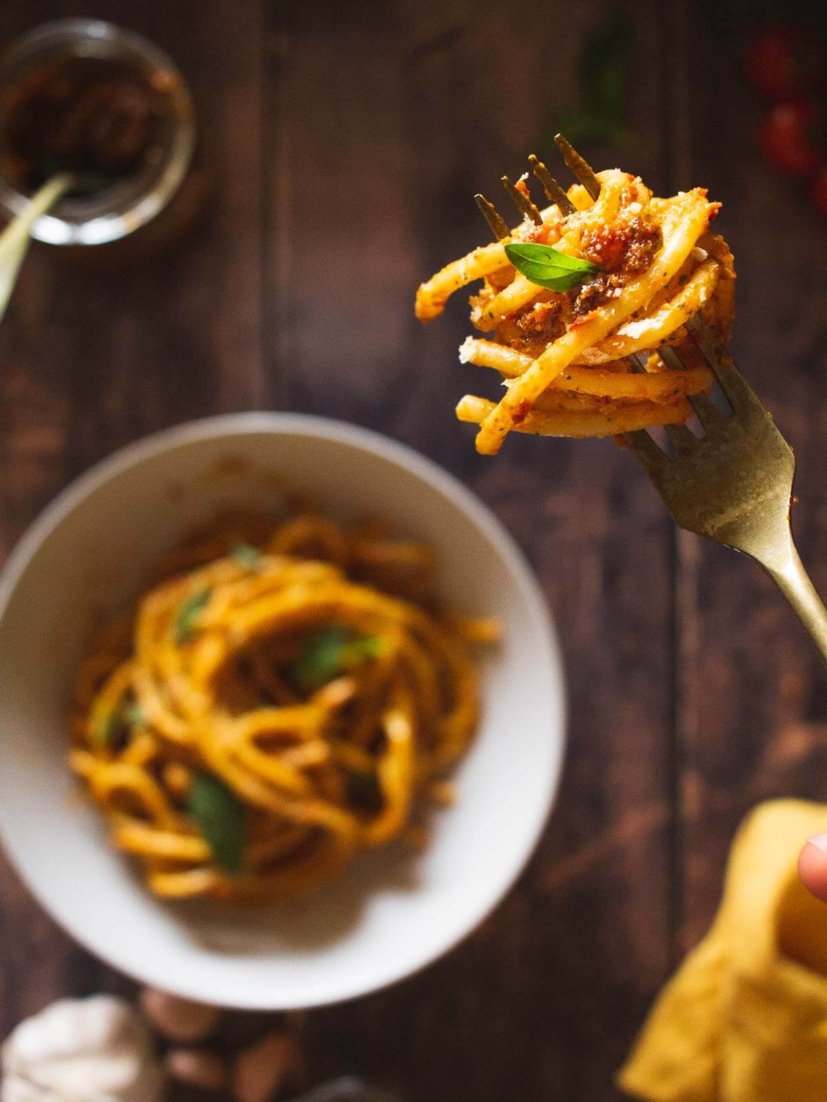 bucatini pasta in a fork holding a bite of sun-dried tomato pesto pasta