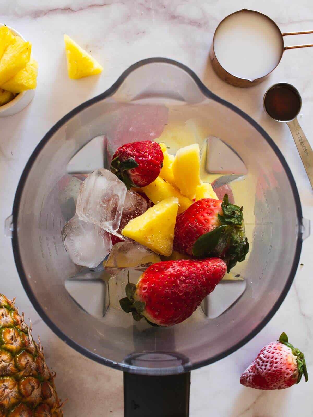 frozen fruit in blender. Next to the blender are the measured almond milk and maple syrup