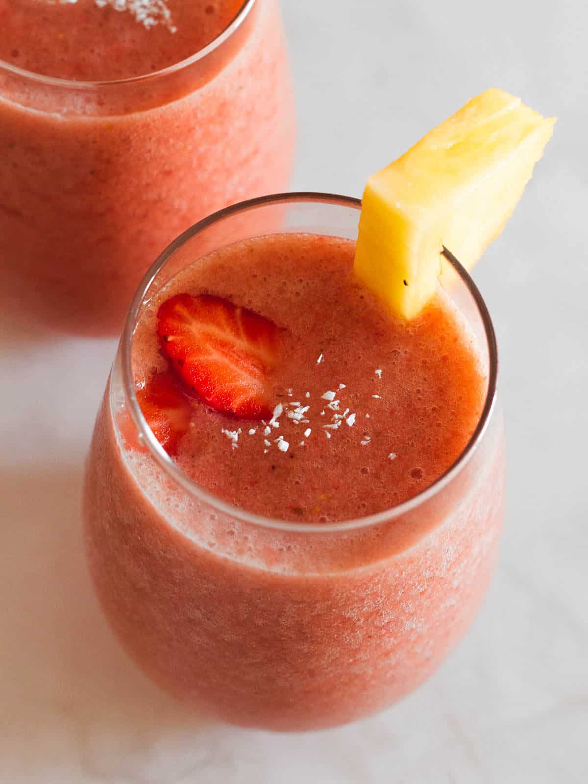 vegan pineapple strawberry smoothie  with shredded coconut on top and garnised with fresh pineapple and strawberry slices