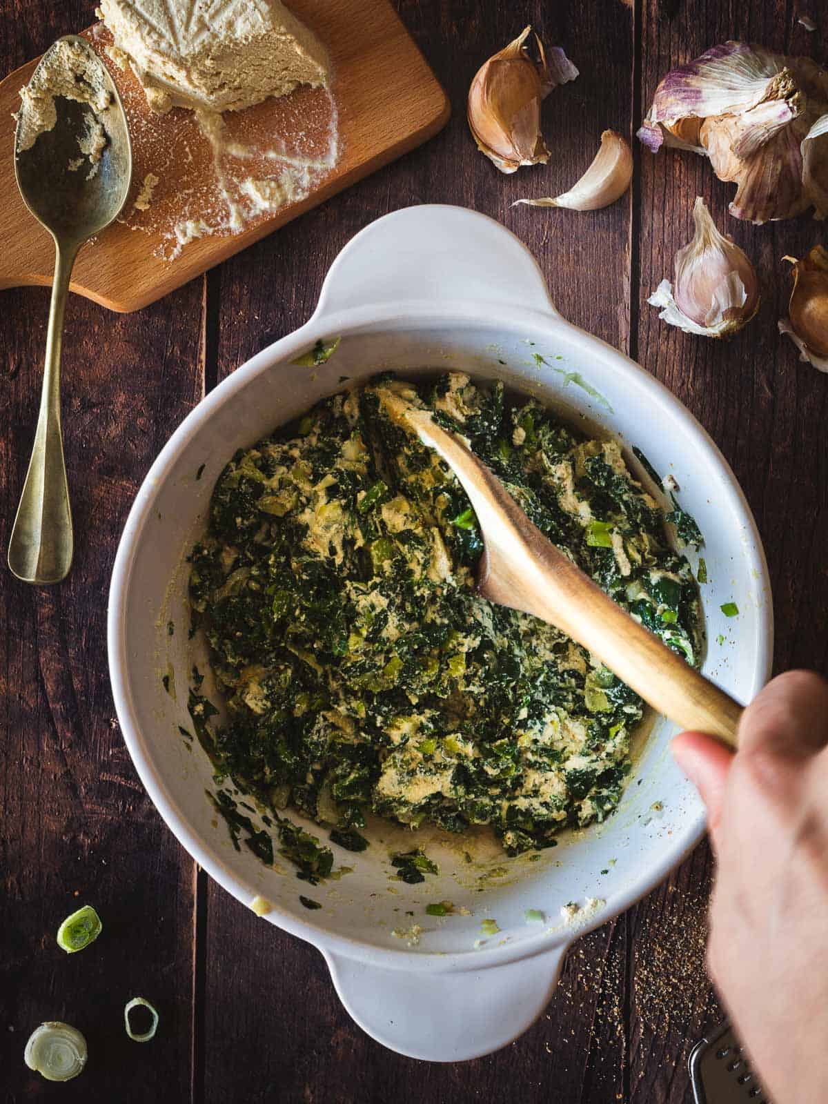 mixing vegan ricotta cheese with cooked spinach mixture