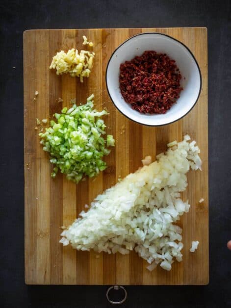 chopped onions, dried tomatoes, and celery, minced garlic on a cutting board