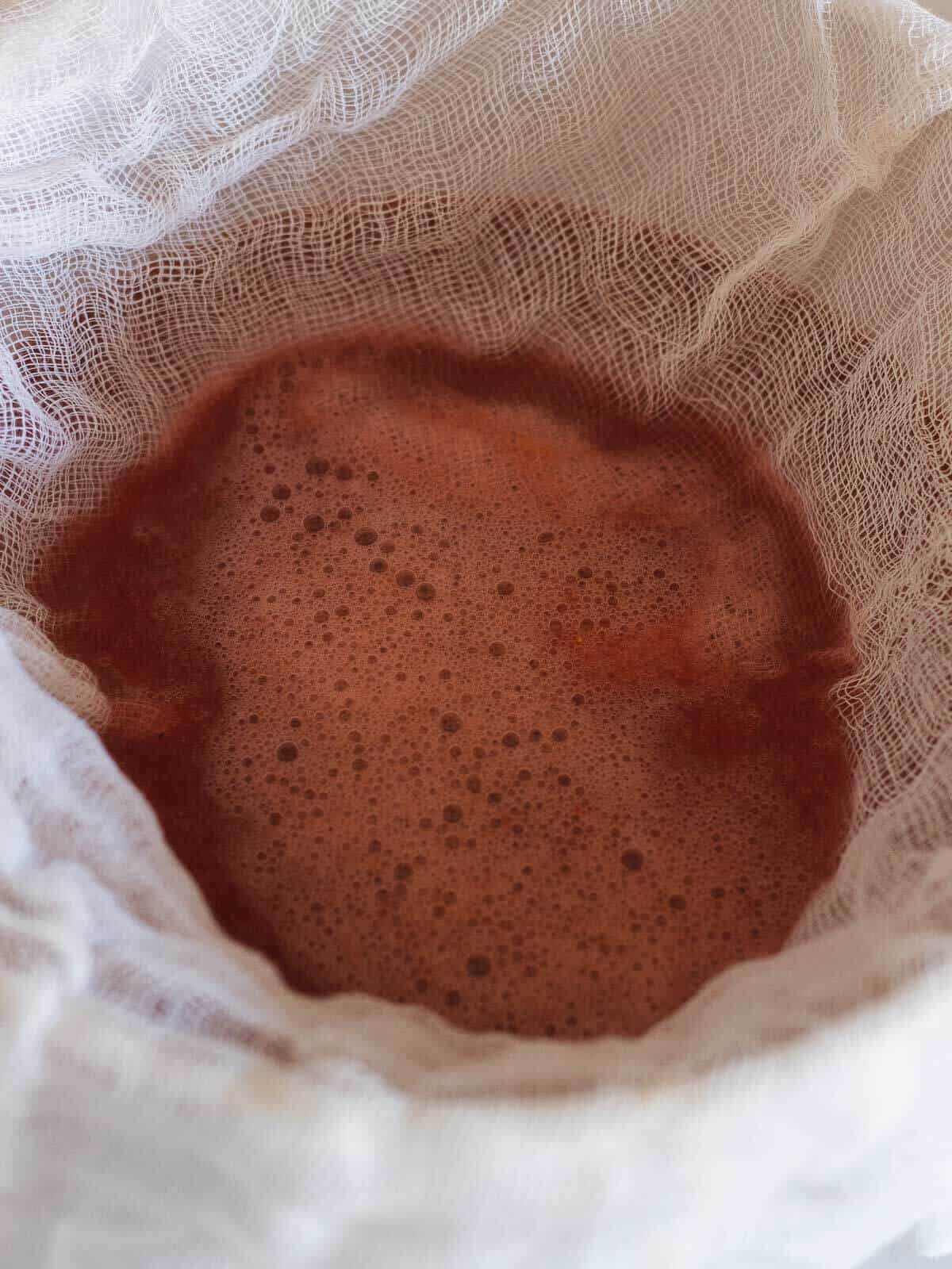 passing strawberry juice through a cheese cloth