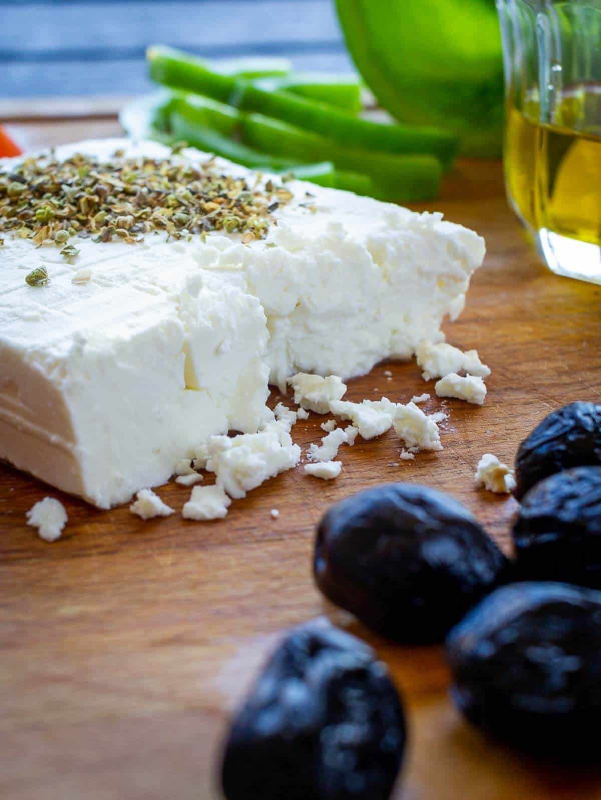 Queso feta vegano y aceitunas negras sobre tabla para cortar.