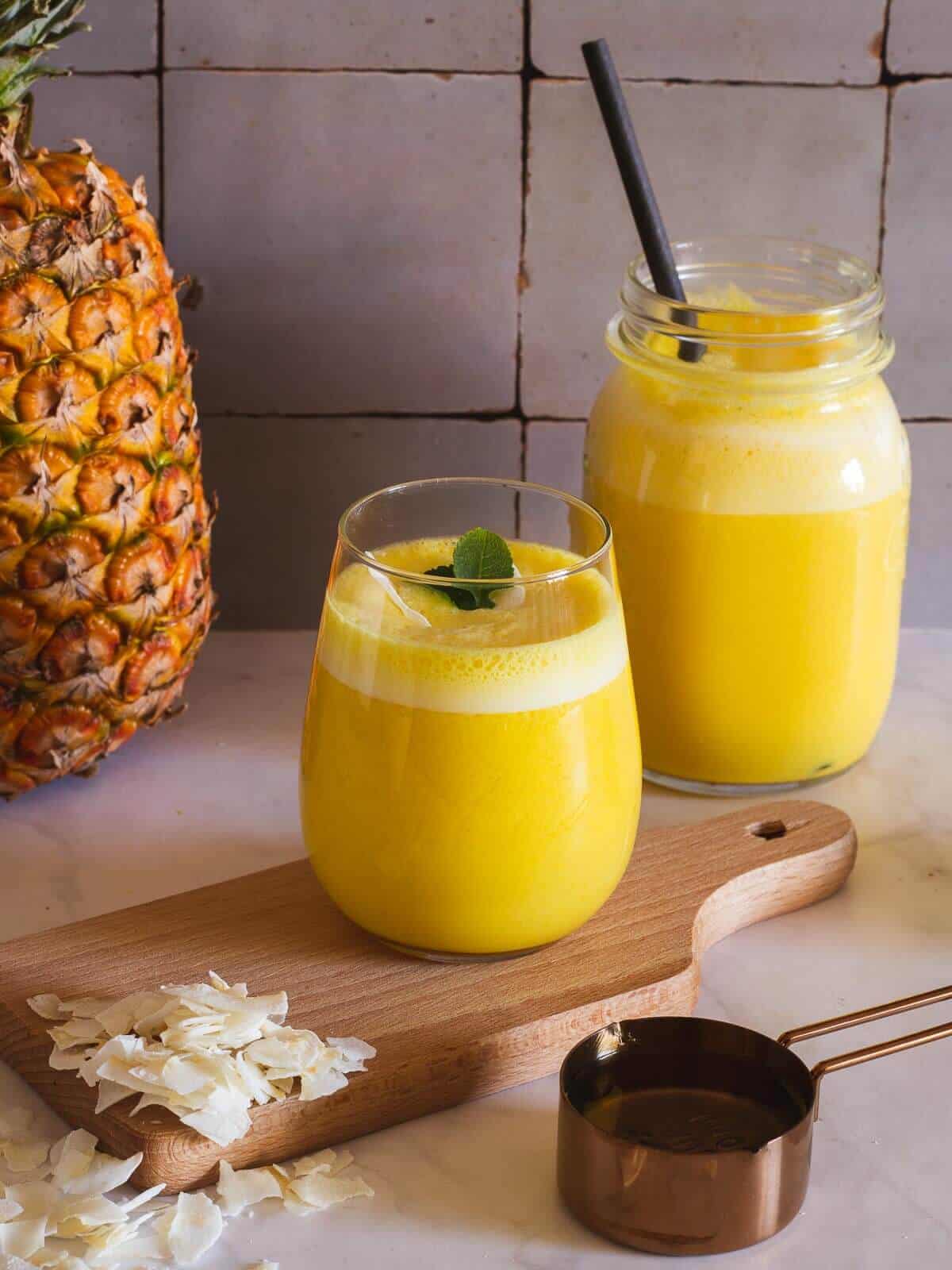 pineapple coconut smoothie in table with maple syrup and coconut flakes