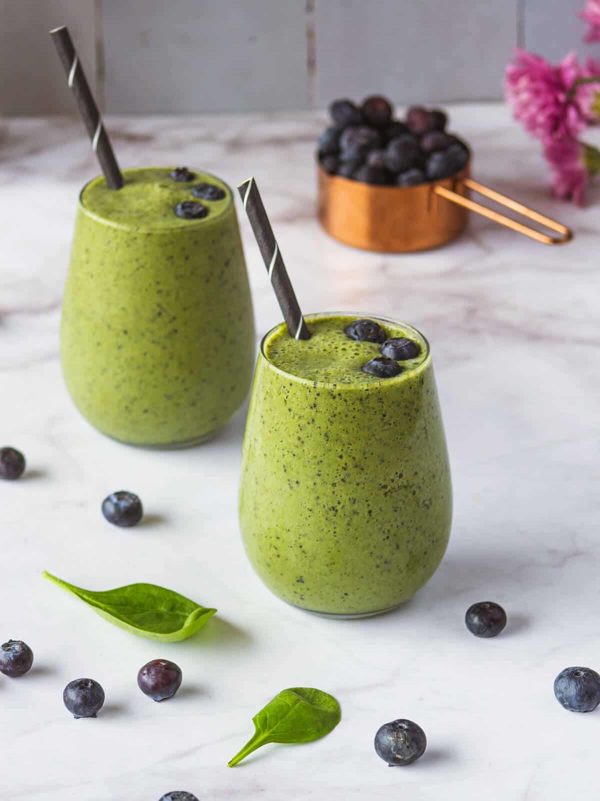 two glasses of Spinach Blueberry Banana Smoothie and a cup of blueberries.