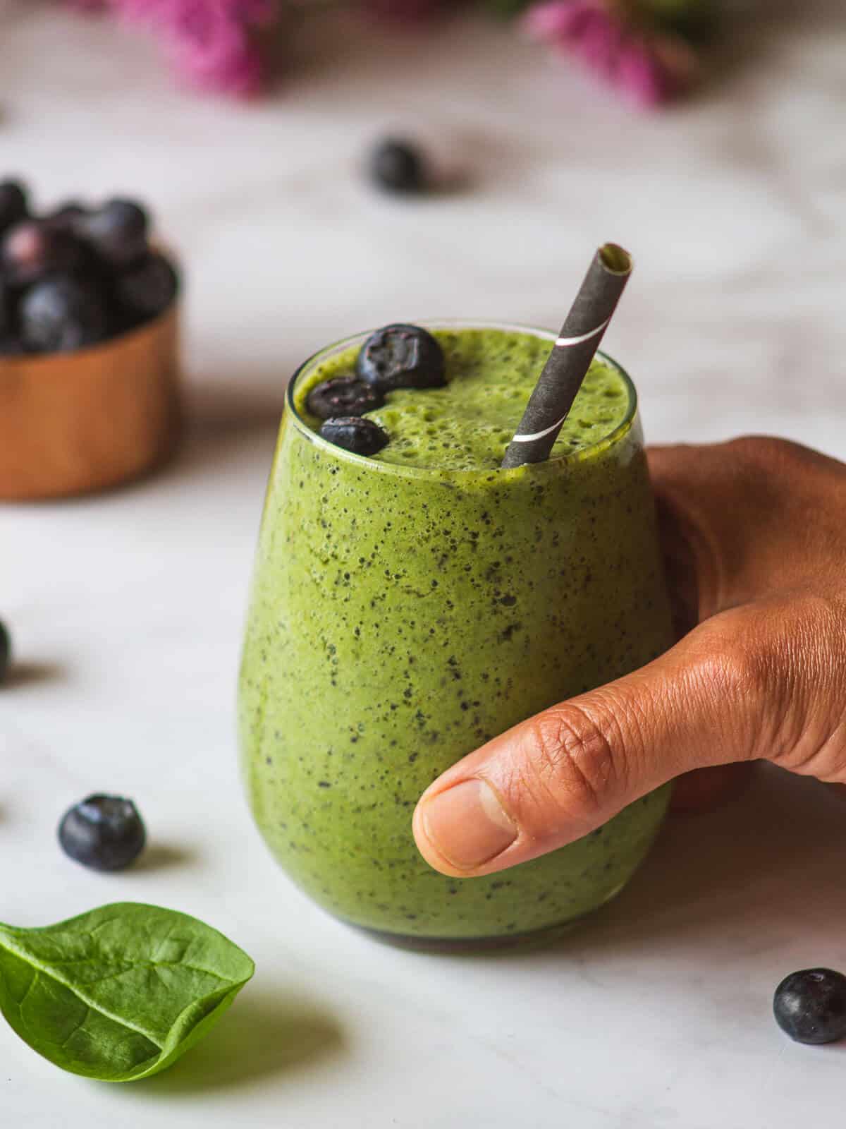 hand holding a glass of blueberry banana smoothie without yogurt