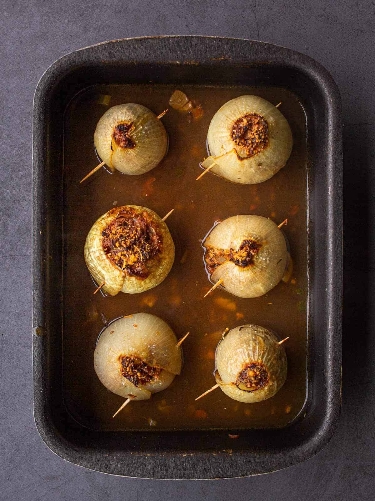 baked onions with toothpick and vegetable stock in a baking dish.
