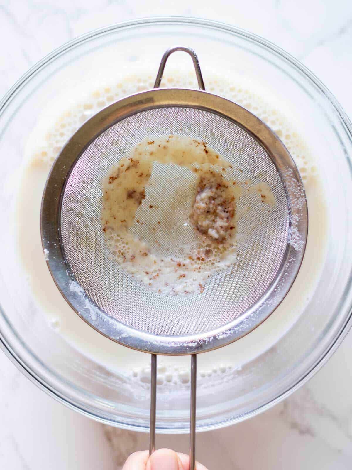 straining cooked soy milk with a wire strainer.