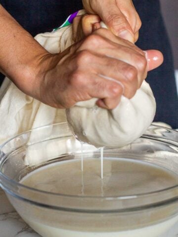 straining oat milk with hand, out of a fine mesh fabric.