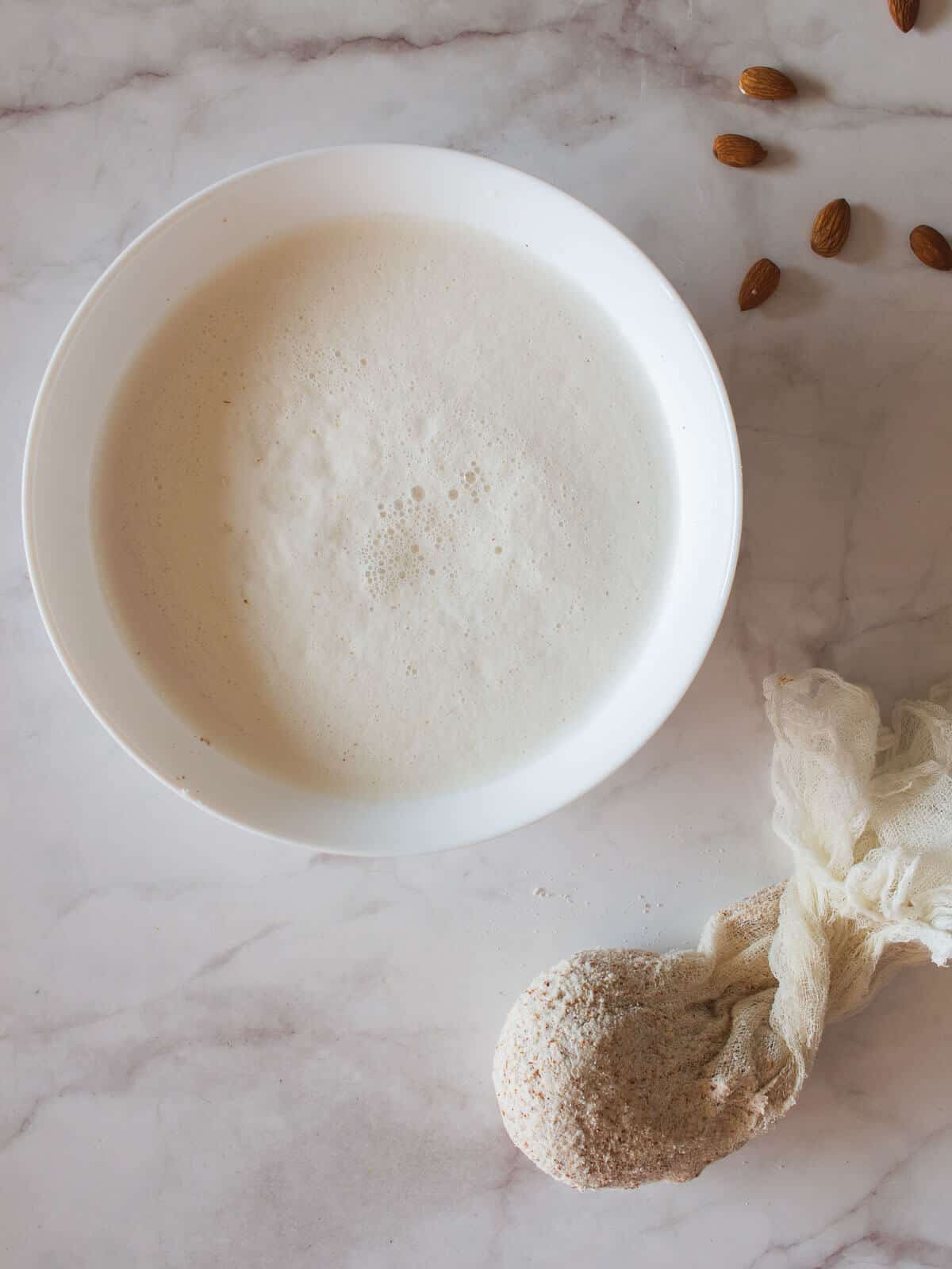 almond milk bowl next to cheesecloth with almond pulp leftovers