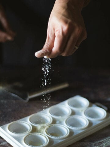 sprinkling flour over a ravioli pasta tray.