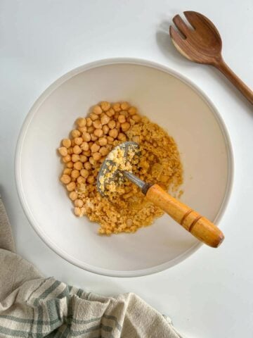 mashing cooked chickpeas with a potato masher.