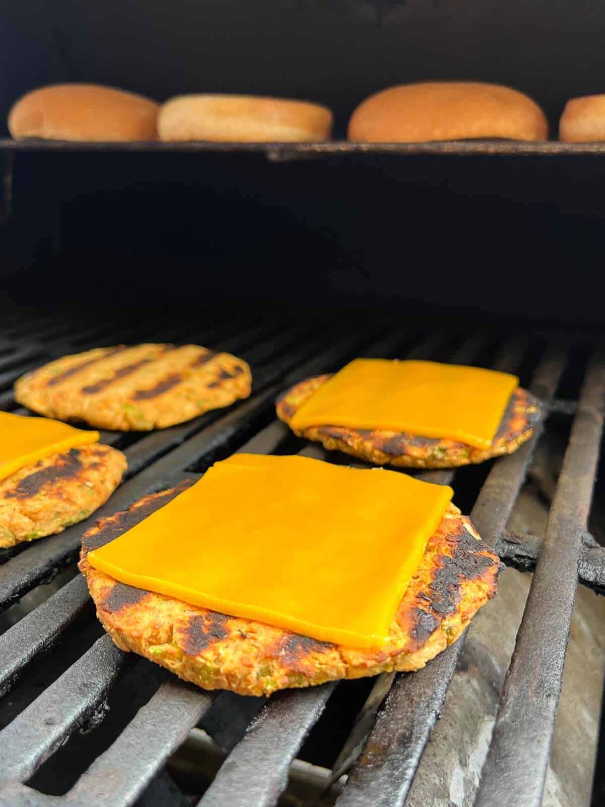 chickpea burgers on a grill with vegan cheddar cheese on top, to allow melting.