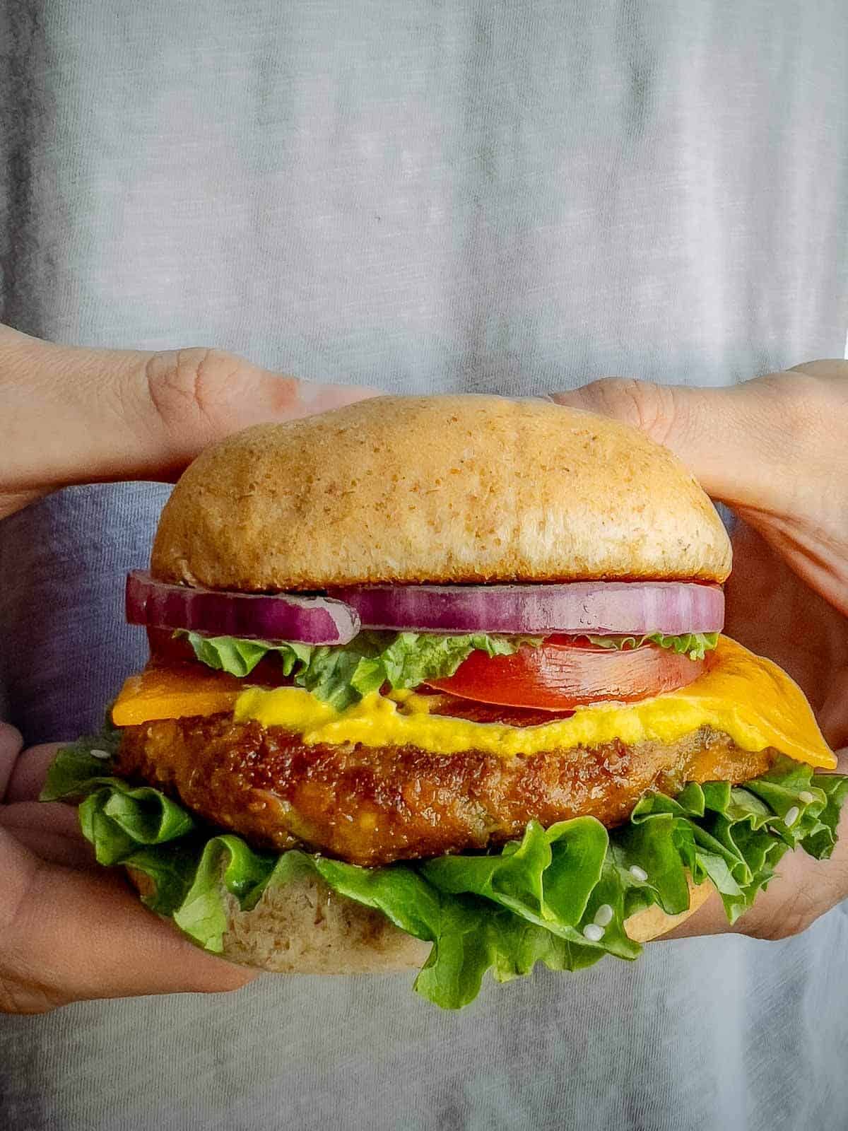 hands holding vegan chickpea burgers with the suggesting add ins, ready to eat.