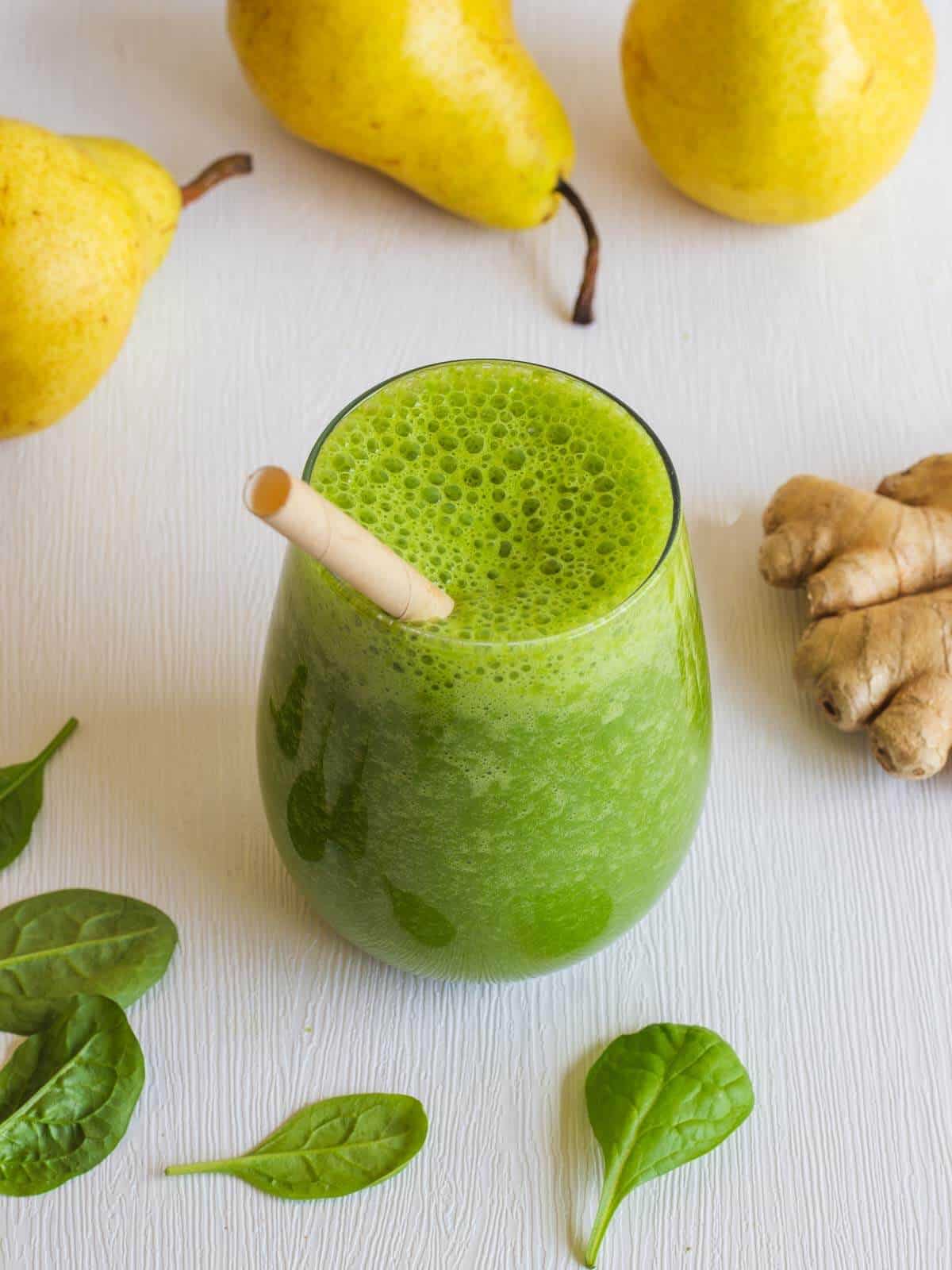 frozen spinach smoothie with ginger root surrounded by spianch leaves, ginger root, and pears.
