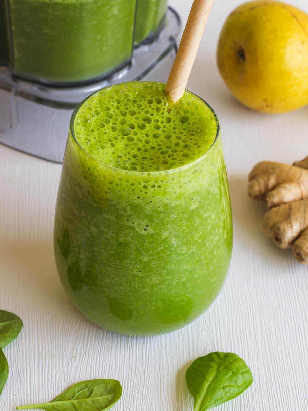 smoothie with ginger served on a table next t the blender, pears, and ginger root.