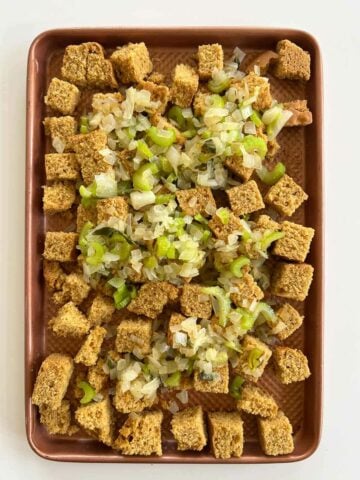 sautéed celery and onions over cornbread dice on a baking sheet.