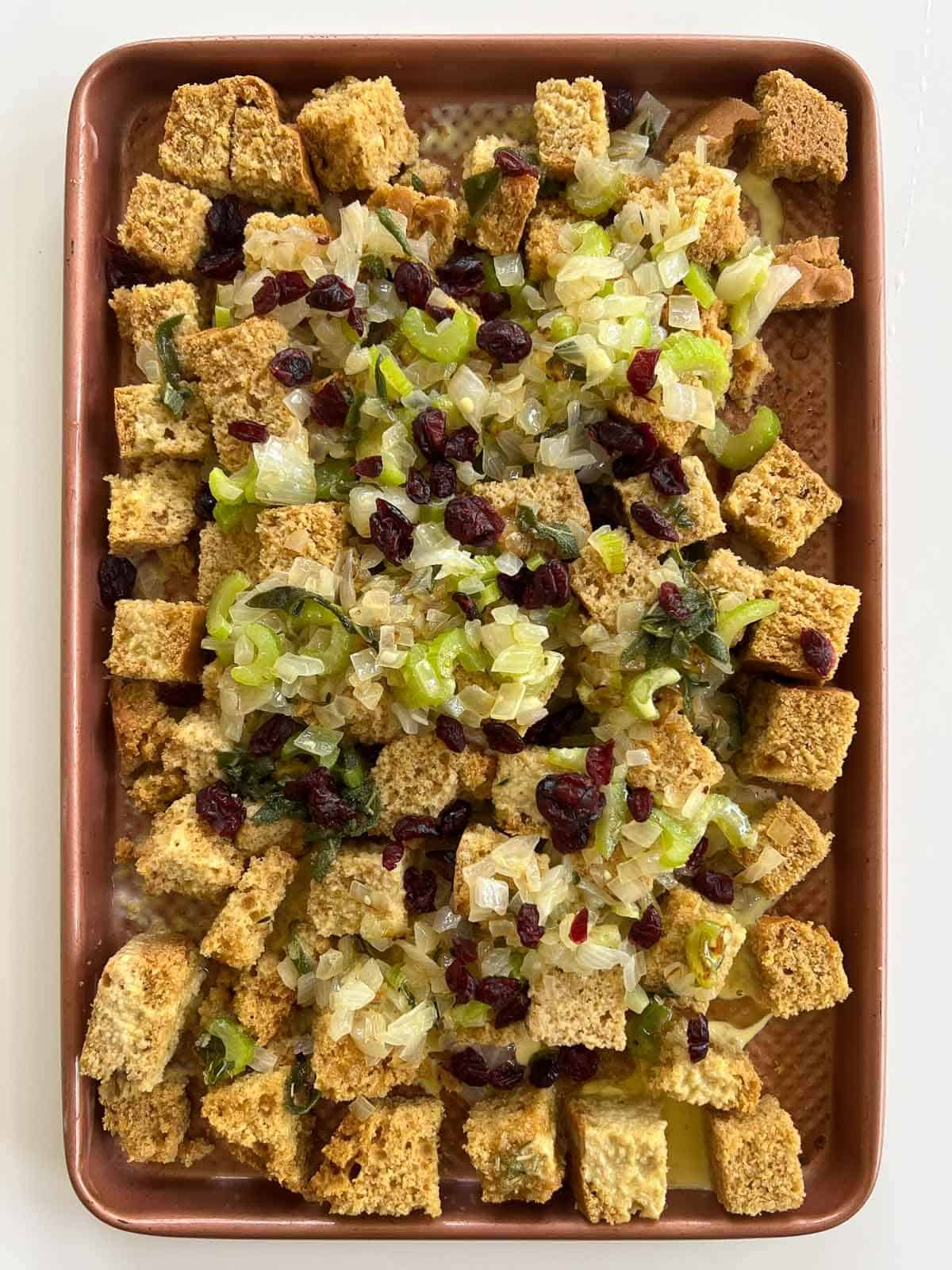 gluten-free cornbread stuffing with cooked vegetables and cranberries on a baking sheet.